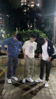 three young men standing next to each other on a brick walkway in front of tall buildings