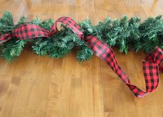 a red and black checkered ribbon is on the floor next to some evergreen branches