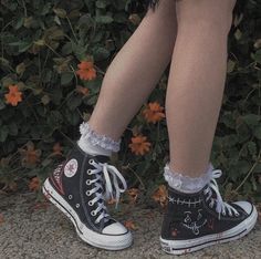 a woman's legs wearing black and white converse shoes with flowers in the background