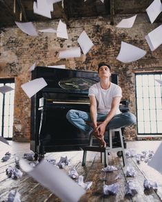 a man sitting on a stool in front of a piano surrounded by paper flying around