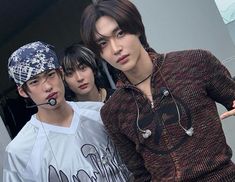 three young men standing next to each other in front of a building with earphones on