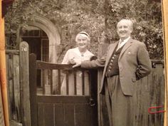 an old black and white photo of two people standing in front of a wooden gate