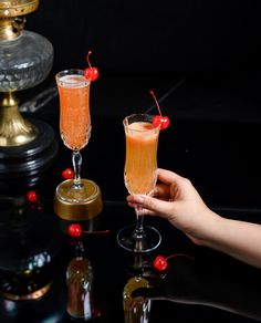 two champagne flutes with cherries on the rim being held by someone's hand