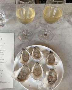 some oysters are sitting on a plate next to two wine glasses and a menu