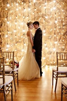 a bride and groom are standing in front of a backdrop with lights on the wall