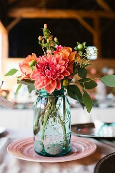 a mason jar filled with flowers on top of a table next to plates and utensils