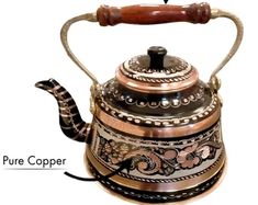 an antique tea kettle with wood handle and ornate designs on the side, labeled as pure copper