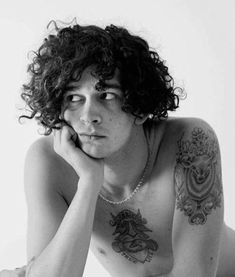 a shirtless man with long curly hair and tattoos on his chest is posing for the camera