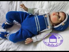 a baby doll laying on top of a white bed covered in blue knitted clothing