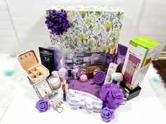 an assortment of beauty products displayed on a white tablecloth with purple flowers in the background