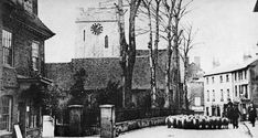 an old black and white photo of sheep walking down the street in front of buildings