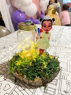 a table topped with a jar filled with plants and a doll sitting on top of it