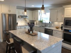 a kitchen with white cabinets and marble counter tops, stainless steel appliances and an island in the middle