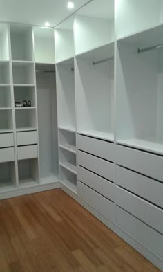 an empty walk in closet with white shelving and wood flooring on the side