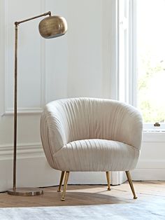 a white chair sitting next to a lamp on top of a hard wood floor in front of a window