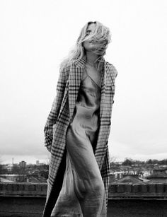 black and white photograph of a woman walking on top of a roof with the city in the background