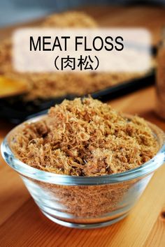 a glass bowl filled with meat floss on top of a wooden table next to other food