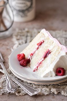 a slice of white cake with raspberries on a plate next to silverware