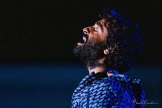 a bearded man singing into a microphone in the dark with his mouth open and eyes closed