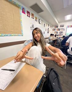 a woman sitting at a desk with her hands in the air and pointing to something