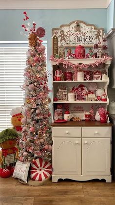 a decorated christmas tree sitting in front of a white hutch with red and pink decorations