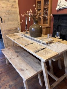 a wooden table with two benches and a vase on it in front of a fireplace