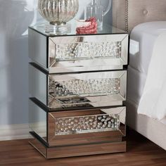 three tiered mirrored shelf with drawers on the bottom and one drawer open, in front of a bed