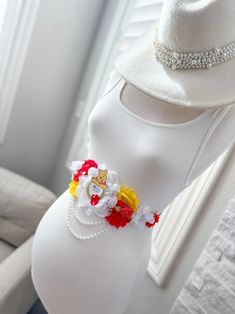 a pregnant woman's belly is adorned with flowers and pearls as she wears a white hat