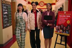 three women standing next to each other in front of a sign that says college fair