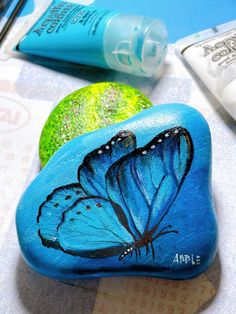 two rocks with blue butterflies painted on them, one is green and the other is blue