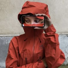 a woman wearing a red raincoat taking a selfie with her cell phone in front of her face