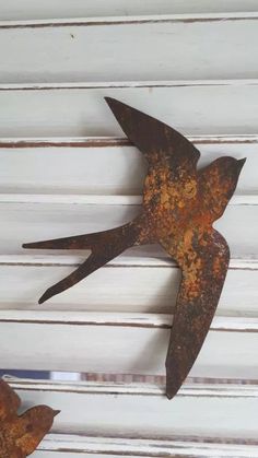 two rusted metal birds sitting on top of a white wall