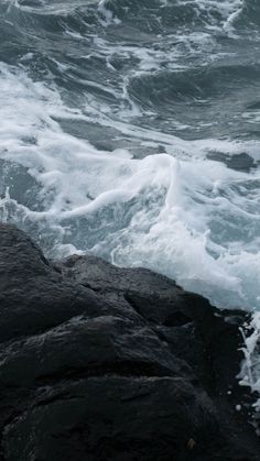 the water is choppy and foamy as it comes up from the rocks near the shore