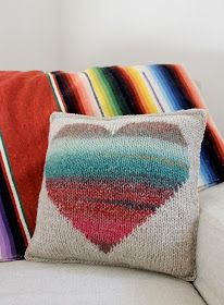 two colorful pillows sitting on top of a white couch next to a pillow with a heart