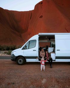 two people standing in front of a van with the door open and mountains behind them