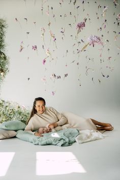 a woman laying on top of a blanket next to a wall with flowers hanging from it