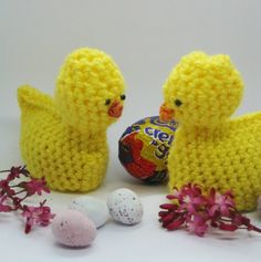 two yellow crocheted ducks sitting next to an easter egg and some pink flowers