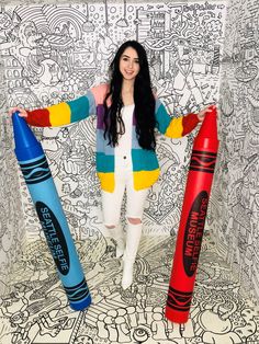 a woman standing next to two giant crayons