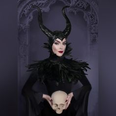 a woman dressed in black holding a skull with horns on her head and wearing a mask