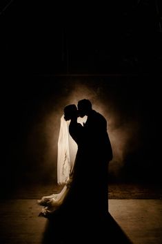 a bride and groom standing in the dark with their arms around each other as they kiss