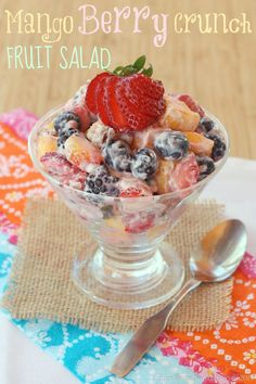 a fruit salad in a glass bowl with a spoon and napkin on the table next to it