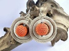 an orange and white crochet earrings hanging from a tree branch on top of a piece of driftwood