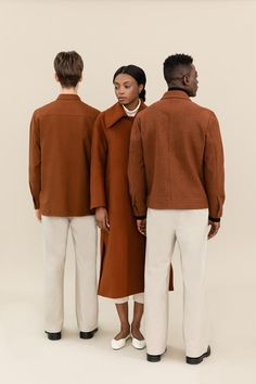 three people standing in front of a white background wearing brown coats and white pants, all looking at the same person