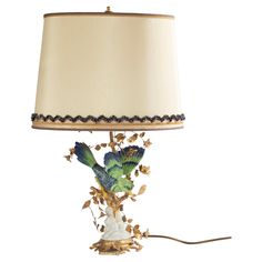 a lamp with a bird on it and leaves around the base that has a white shade