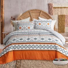 a bed with an orange and white comforter on top of it next to a basket