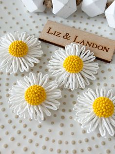 four white and yellow flowers are sitting on a table next to some cotton cubes