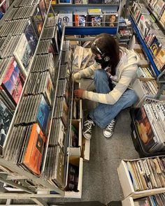 a woman sitting on the floor in front of a shelf filled with records and cds