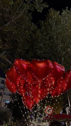 large red balloons are floating in the air on a city street at night with trees and buildings behind them