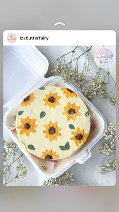 a cake with sunflowers on it sitting in a plastic container next to flowers