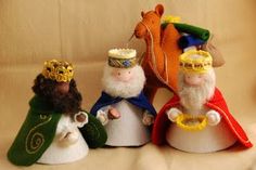 three small christmas figurines are sitting on a white cloth covered surface, one is wearing a gold crown and the other has a green cape